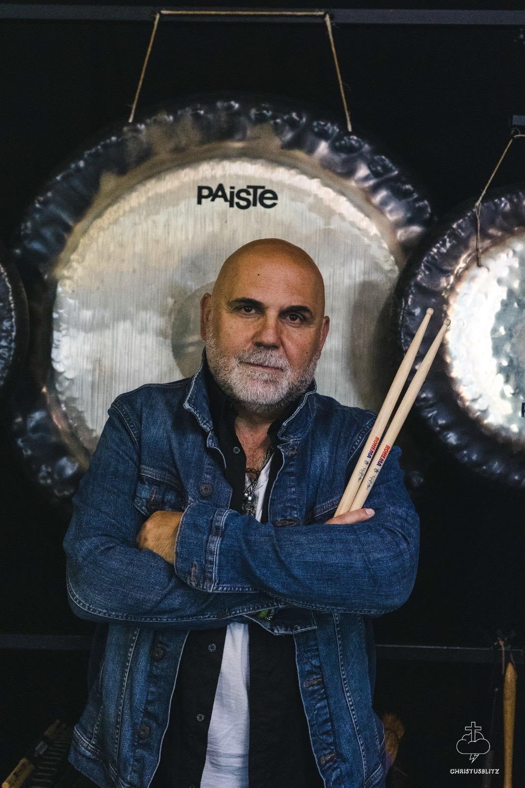 Tony Liotta with drumsticks in front of large Paiste gongs
